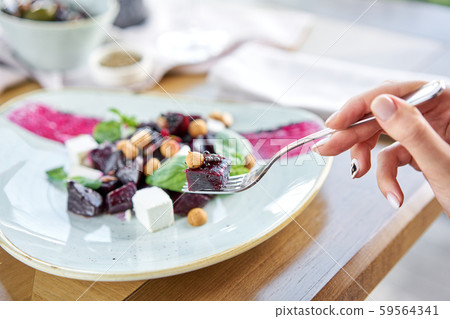Woman eats Italian salad with beetroot, basil leaves and cheese feta, with oil and small 59564341