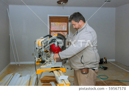 Worker cuts wood baseboard on the power saw Worker cuts wood baseboard on the power saw 59567578