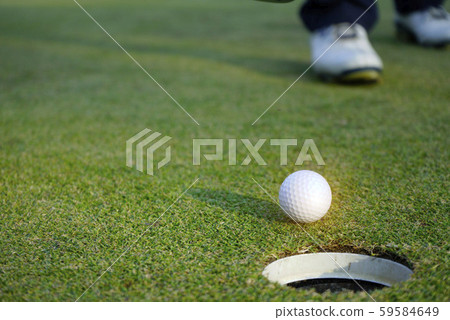 White golf ball near hole on green grass. White golf ball near hole on green grass. 59584649