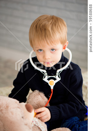 Cute little boy dressed as doctor playing with toy bear at home. Cute little boy dressed as doctor playing with toy bear at home. 59588688