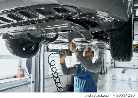 Competent mechanic in blue overalls repairing car suspension 59594280