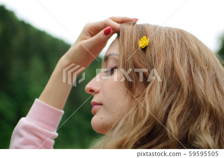 Outdoors portrait of young calm blonde woman in pink clothes with little yellow flower in her long 59595505