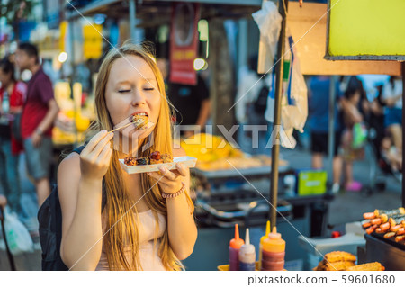 Young woman tourist eating Typical Korean street food on a walking street of Seoul. Spicy fast food Young woman tourist eating Typical Korean street food on a walking street of Seoul. Spicy fast food 59601680