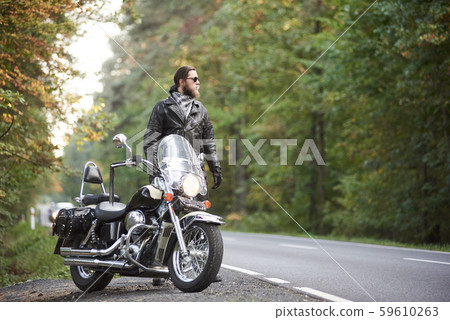Tall athletic biker in black leather clothing standing at modern powerful high-speed motorcycle. Tall athletic biker in black leather clothing standing at modern powerful high-speed motorcycle. 59610263