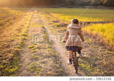 一個女孩在日落的路上騎自行車 59613198