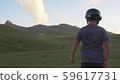 a boy in a motorcycle helmet walks on a hillside against the backdrop of mountains backlit by sunset 59617731