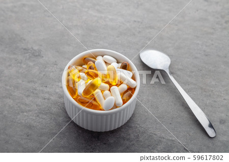 Scattered medicine vitamins, pills, drugs in bowl with metal spoon on gray background. White food 59617802