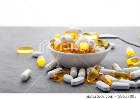 Scattered medicine vitamins, pills, drugs in bowl with metal spoon on gray background. White food 59617803