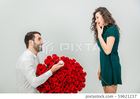 Man asking partner to marry him by giving her a engagement ring and bunch of red flowers, woman is Man asking partner to marry him by giving her a engagement ring and bunch of red flowers, woman is 59621237