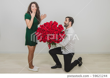 Man asking partner to marry him by giving her a engagement ring and bunch of red flowers, woman is Man asking partner to marry him by giving her a engagement ring and bunch of red flowers, woman is 59621244