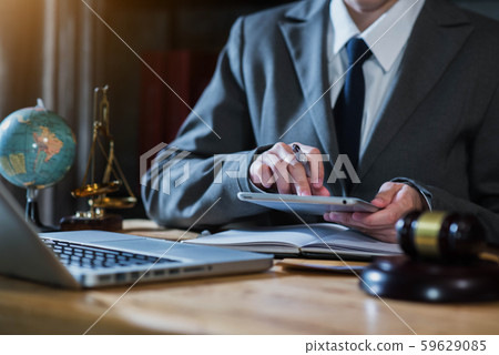 Justice and law concept.Male judge in a courtroom the gavel, working with digital tablet computer on wood table in sun light. 59629085