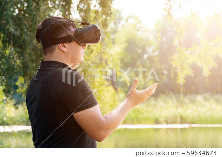 Smile happy man getting experience using VR-headset glasses of virtual reality in nature summer 59634673