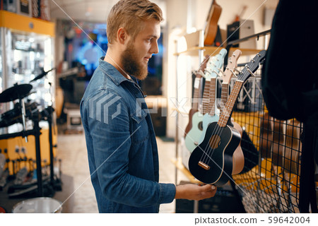 Young man choosing ukulele guitar in music store 59642004
