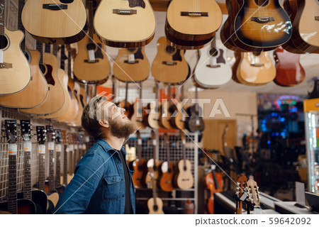 Young guy choosing acoustic guitar in music store 59642092