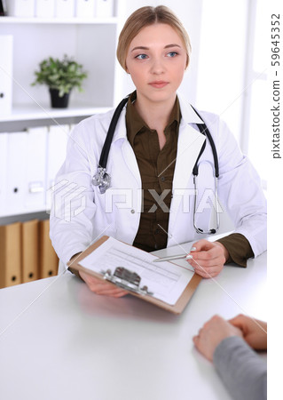 Young woman doctor and patient at medical examination in hospital office. Khaki colored blouse of 59645352
