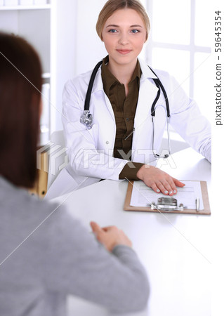 Young woman doctor and patient at medical examination in hospital office. Khaki colored blouse of 59645354