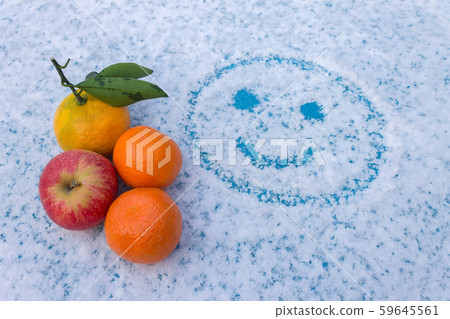 A set of fruits lies on a snowy table with a painted, smiling face A set of fruits lies on a snowy table with a painted, smiling face 59645561