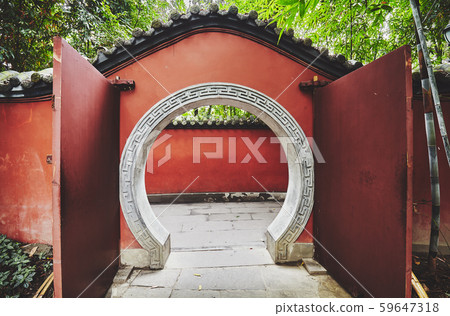 Round gate in red wall passage, China. 59647318