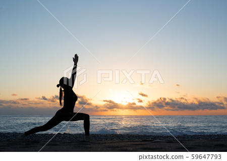 Female silhouette doing yoga on the beach in front of rising sun, warrior pose, hands up 59647793