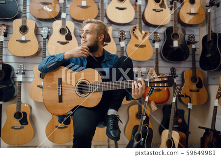 Young man plays on acoustic guitar in music store 59649981