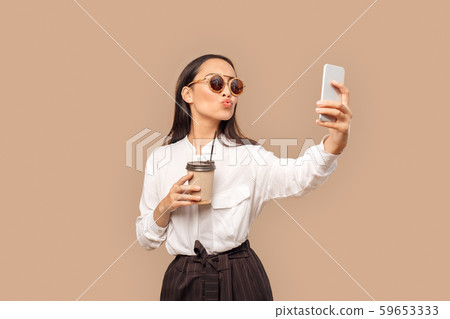 Freestyle. Young woman in shirt and sunglasses standing isolated on bage with cup of coffee taking 59653333