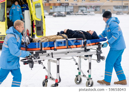 Two paramedics pushing sick unconscious man on stretcher towards ambulance car Two paramedics pushing sick unconscious man on stretcher towards ambulance car 59658043