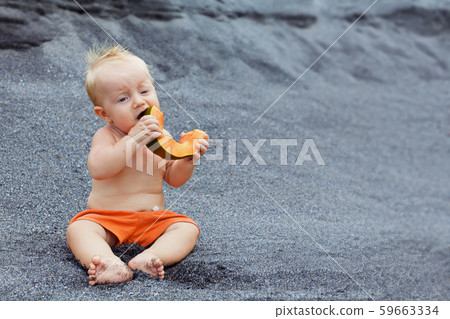 Happy baby boy eating orange papaya fruit on black Happy baby boy eating orange papaya fruit on black 59663334