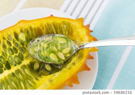 Spoon in half of orange kiwano (cucumis metuliferus, horned melon) on white saucer. Spoon in half of orange kiwano (cucumis metuliferus, horned melon) on white saucer. 59686158