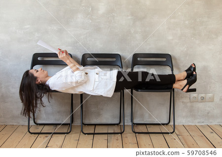 Woman in casual clothing lays on chairs and reading text from sheet of paper Woman in casual clothing lays on chairs and reading text from sheet of paper 59708546
