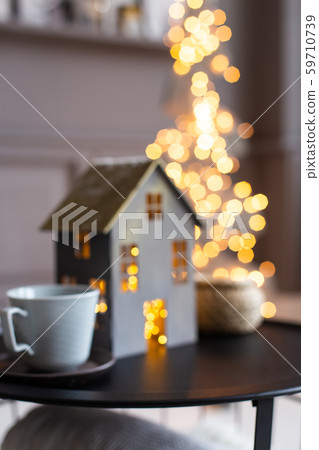 Closeup blurred photo of lighted from inside christmas decorative house and two cups standing on 59710739