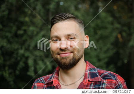 Close up portrait of young bearded man in red shirt looking at the camera with smile in the park on Close up portrait of young bearded man in red shirt looking at the camera with smile in the park on 59711027