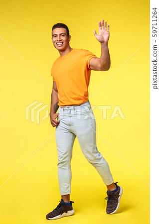 Vertical full-length studio shot friendly young handsome man smiling, waving raised hand outgoing as Vertical full-length studio shot friendly young handsome man smiling, waving raised hand outgoing as 59711264