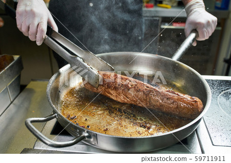 The chef works in the kitchen of the restaurant. Fresh meat roasted in a large frying pan 59711911