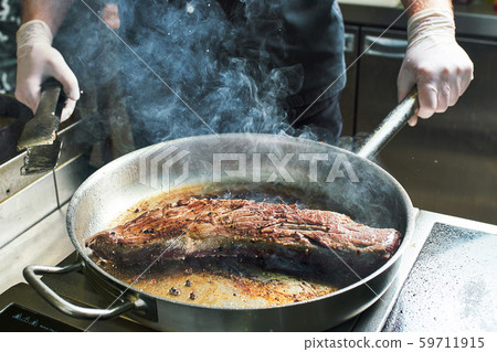 The chef works in the kitchen of the restaurant. Fresh meat roasted in a large frying pan The chef works in the kitchen of the restaurant. Fresh meat roasted in a large frying pan 59711915