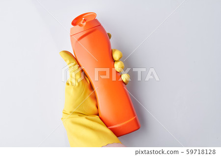 Hand in glove holding orange bottle detergent. 59718128