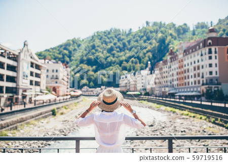 Happy girl at hat on the embankment of a mountain river in a European city. Happy girl at hat on the embankment of a mountain river in a European city. 59719516