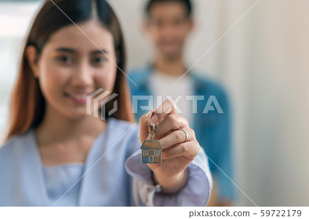 Closeup Asian young woman hand holding the house key chain over the photo blurred of lover carrying big cardboard box for moving in new house after sign contact, Moving and House Hunting concept 59722179