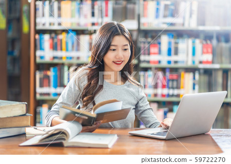 Asian young Student in casual suit doing homework and using technology laptop in library of university or colleage with various book and stationary over the book shelf background, Back to school 59722270