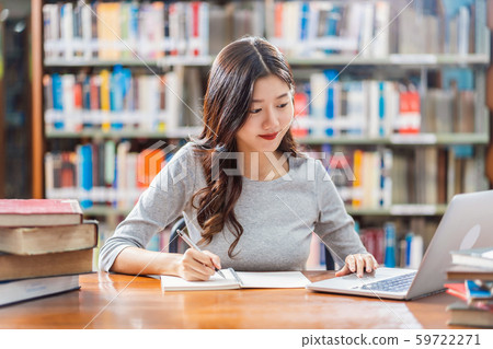 Asian young Student in casual suit doing homework and using technology laptop in library of university or colleage with various book and stationary over the book shelf background, Back to school 59722271
