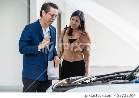Asian receptionist open the car hood for checking and explaining the basic list of maintain to customer at maintainance service center for in showroom Asian receptionist open the car hood for checking and explaining the basic list of maintain to customer at maintainance service center for in showroom 59722304