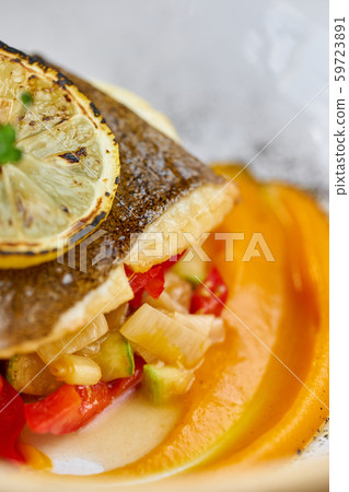 Closeup Roasted pike perch or cod fish with baked vegetables. Dish decorated with a slice of lemon 59723891