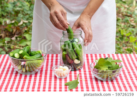 Woman's hands put cucumber in glass jar for preservation Woman's hands put cucumber in glass jar for preservation 59726159