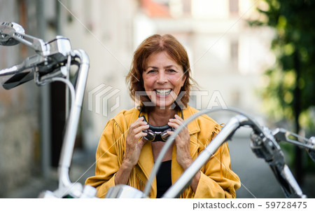 Cheerful senior woman traveller with motorbike in town. Cheerful senior woman traveller with motorbike in town. 59728475