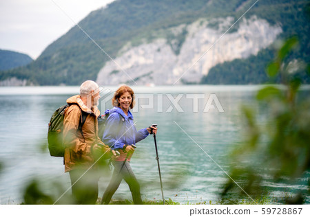 A senior pensioner couple hiking by lake in nature, talking. 59728867