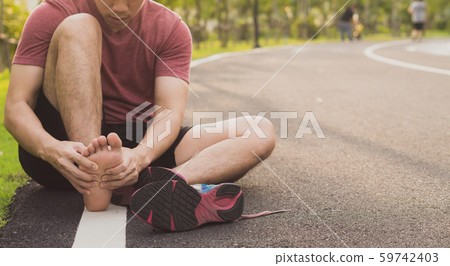 Young man massaging his painful foot from jogging and running at park. Sport and exercise concept. Young man massaging his painful foot from jogging and running at park. Sport and exercise concept. 59742403