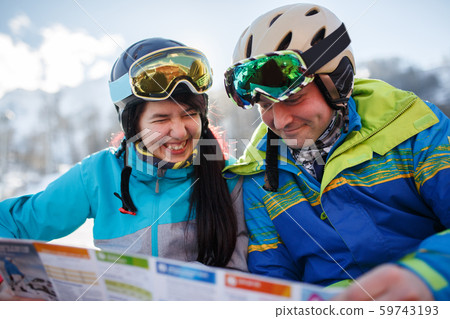 Smiling woman and man in helmet with map in hands at snow resort on winter day 59743193