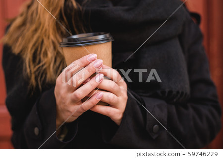 Female hand with paper cup of coffee take away. Woman holding cup on the red wall. Sunny afternoon. 59746229