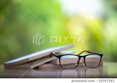 Black eyeglasses with books on wooden table, Bokeh garden background, Close up & Macro shot, Selective focus, Stationery concept 59747543