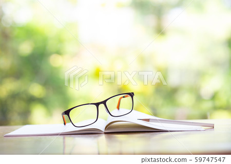 Black eyeglasses, white pencil with white notebook on wooden table, Bokeh garden background, Close up & Macro shot, Selective focus, Stationery concept 59747547