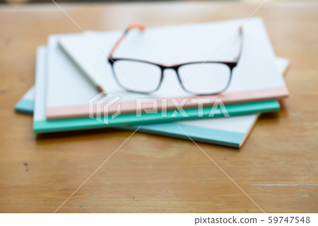 Blurred black eyeglasses, white pencil with three white notebooks on wooden table, Close up & Macro shot, Stationery concept 59747548